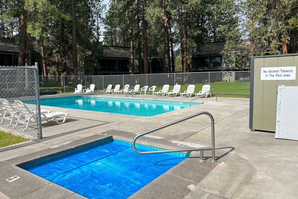 A swimming pool with lounge chairs, a no alcohol/tobacco sign, and a fenced area.