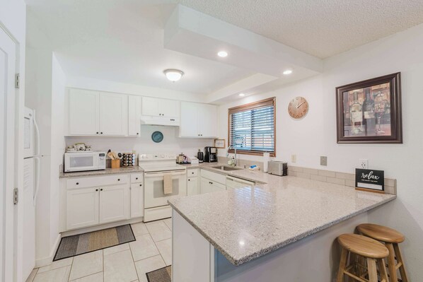 A modern kitchen with white cabinets, a granite countertop, a built-in oven, a microwave, and a coffee maker.