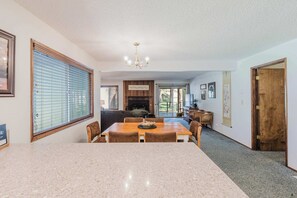 A dining area with a marble table, wooden chairs, a chandelier, and a fireplace in the background. - Delightful escape near downtown with shared pool & hot tub, rec room, & large deck (Sisters)