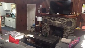 Ein Wohnzimmer mit Kamin aus Stein, einem darüber hängenden Fernseher, einem Sofa und einem Couchtisch.