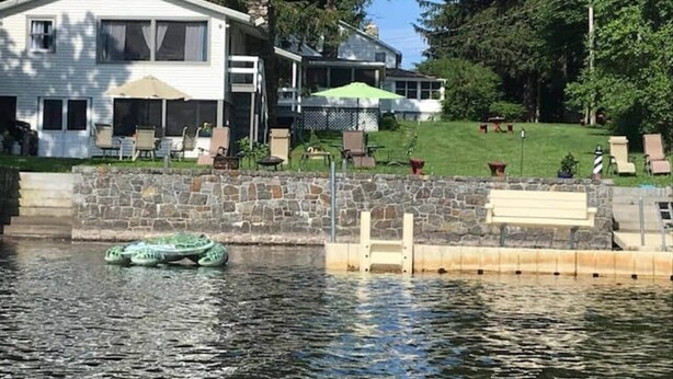 Ein Haus mit einem Steg, der sich ins Wasser erstreckt, einer Steinmauer und Gartenmöbeln.