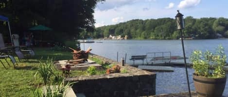 Un patio junto al lago con un banco de piedra, una planta en maceta y un farol.