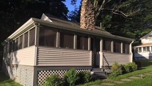 Ein zweistöckiges Haus mit einem Steinsschornstein, einer Veranda und einem umzäunten Garten.