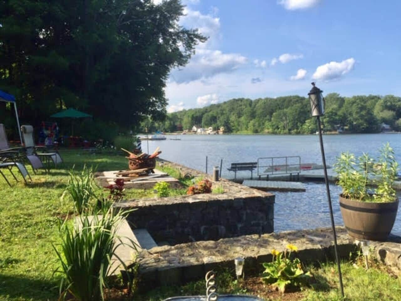 Un patio junto al lago con un banco de piedra, una planta en maceta y un muelle que se adentra en el agua.