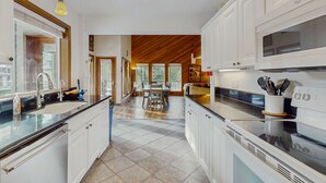 Una cocina moderna con armarios blancos, encimera negra y comedor con mesa y sillas de madera.