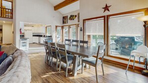 Amplia sala de estar con mesa de comedor, sillas, sofá, ventilador de techo y ventanas grandes con vistas.