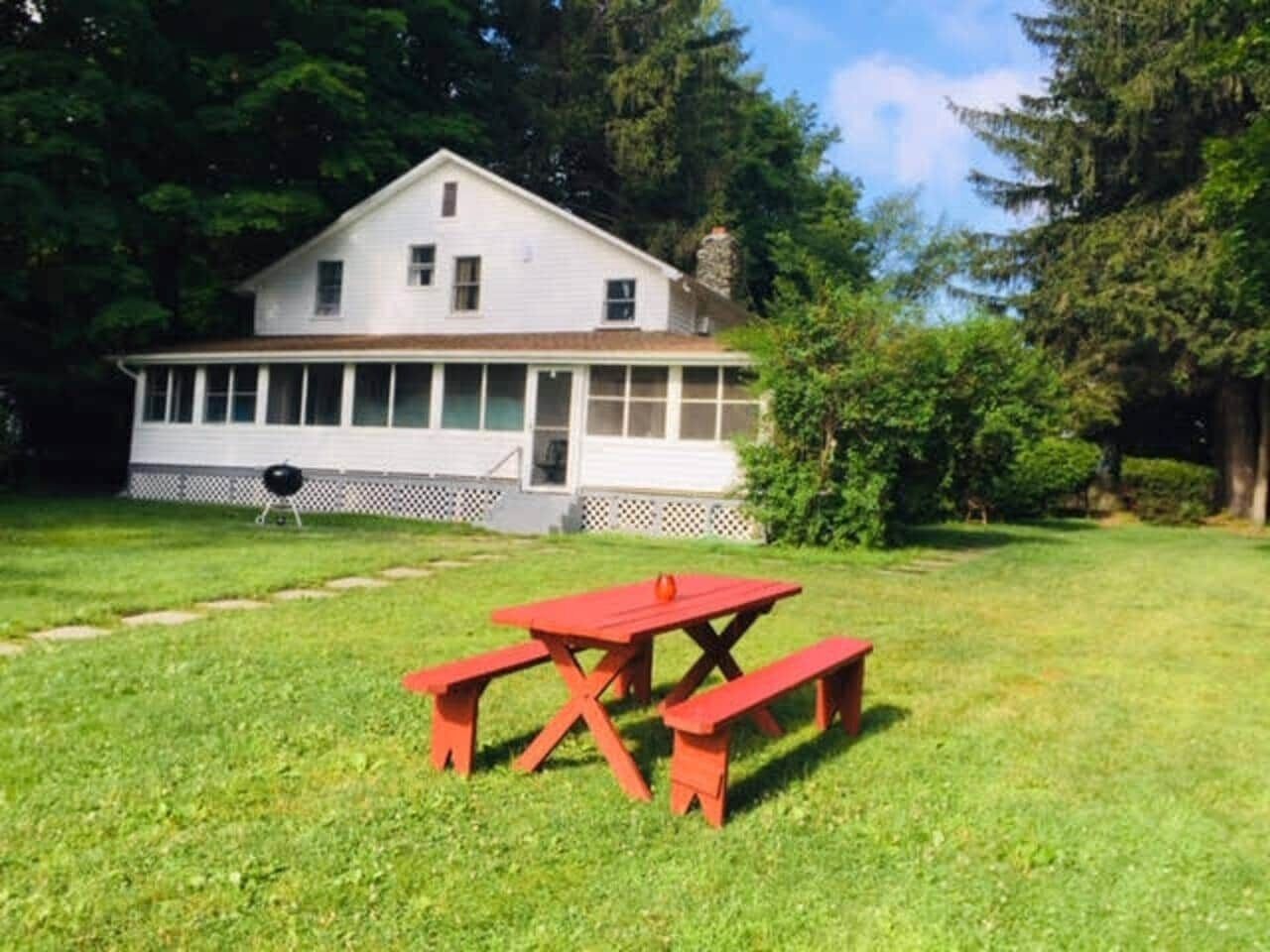 Ein Haus mit Veranda, einem roten Picknicktisch und einem Grill.