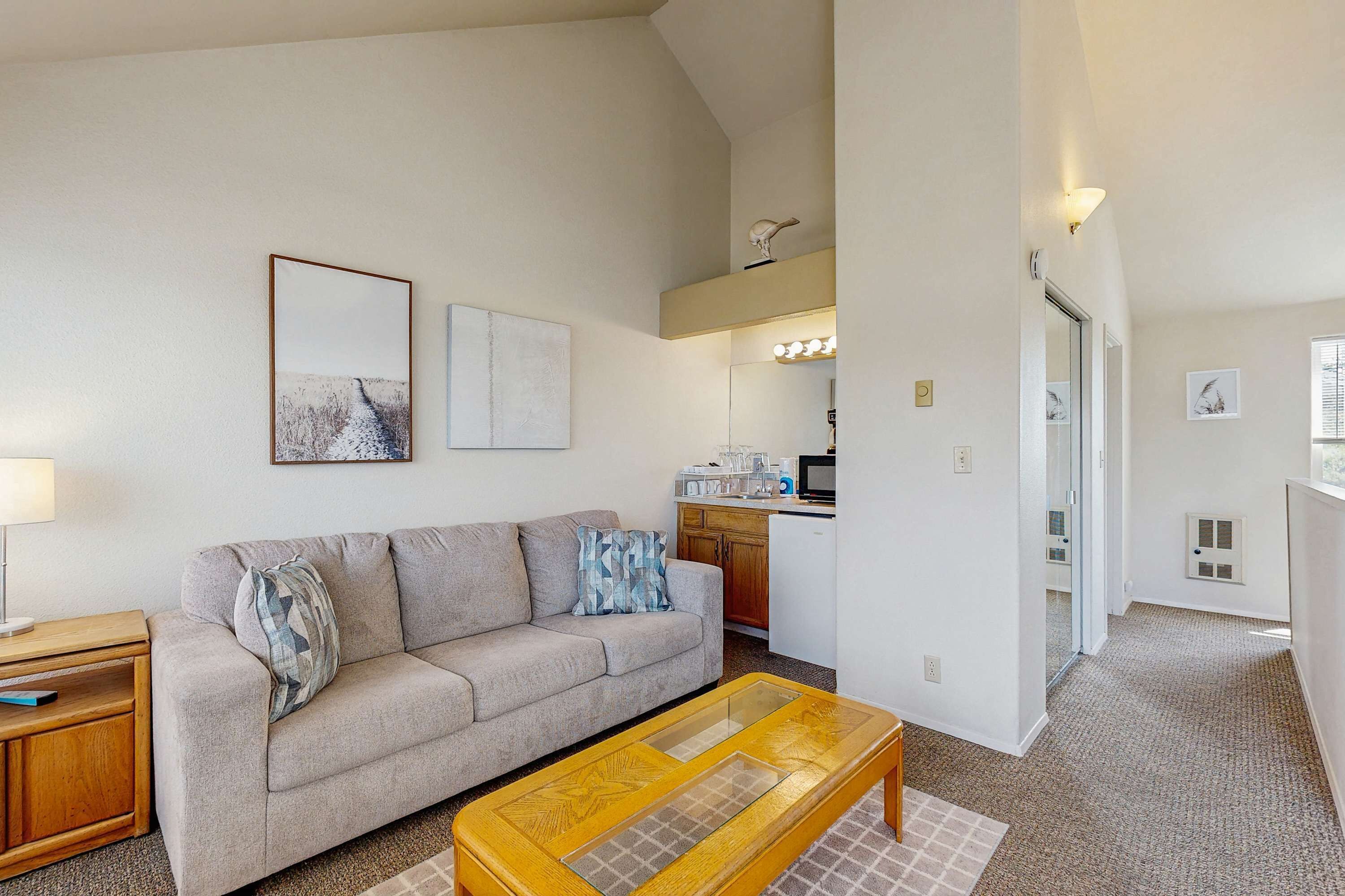A living room with a sofa, coffee table, and a kitchen in the background.