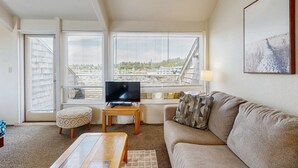 Ein Wohnzimmer mit einer Couch, Hocker, Fernseher und Blick auf eine Brücke.