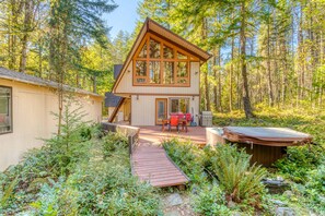 A two-story cabin with a deck, surrounded by dense forest. - Dog-friendly, A-frame cabin with private hot tub - tranquil setting near skiing (Welches)