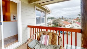 A wicker chair with cushions on a balcony with a red railing, overlooking a street with houses and a cloudy sky. - Classy and Convenient Dog-Friendly Condo with Private Balcony (Florence)