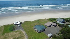 An aerial view of a coastal property with a beach, a circular building, and several other structures. - Dog-friendly oceanfront beach home with private hot tub and stunning ocean views (Yachats)