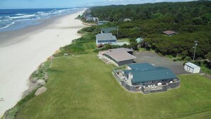 An aerial view of a coastal property with a large building, a parking area, and a beach. - Dog-friendly oceanfront beach home with private hot tub and stunning ocean views (Yachats)