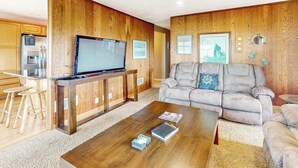 A living room with a wooden wall panel, a sofa, a coffee table, and a television. - Dog-friendly oceanfront beach home with private hot tub and stunning ocean views (Yachats)