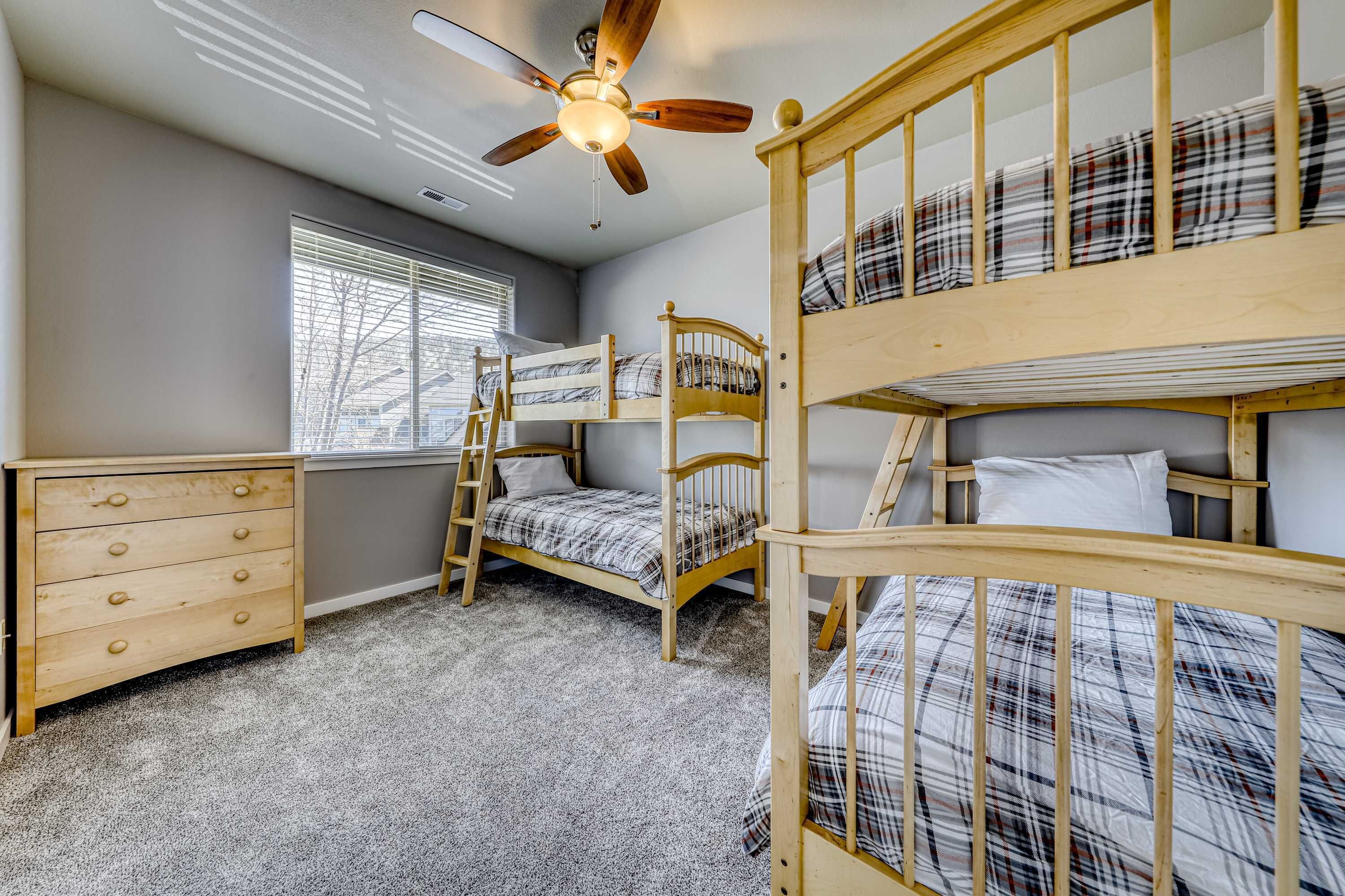 Ein Zimmer mit Etagenbetten, einer Holzkommode, einem Deckenventilator und einem Fenster mit Jalousien.
