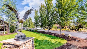 A landscaped area with a stone pedestal, a metal sculpture of an eagle, and a well-maintained lawn. - Two-Story Townhouse withFree WiFi, Fireplace, AC, Patio, & Shared Hot Tub, Pools (Eagle Crest)