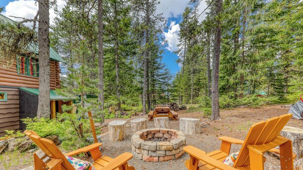 Eine Blockhütte mit Feuerstelle und Adirondack-Stühlen in einer Waldlandschaft.