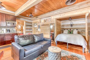 A log cabin interior with a kitchenette, a leather sofa, a bed, and a rustic wooden ceiling. - Adorable studio with modern amenities - close to slopes & restaurants (Government Camp)