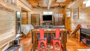 Ein Holzblockhaus-Interieur mit Esstisch, roten Stühlen, einer Couch, einem Fernseher und einem Kamin.