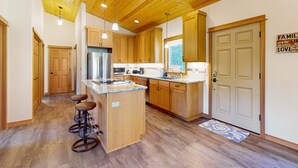 Una cocina con armarios de madera, un refrigerador de acero inoxidable, una isla central con taburetes y techo de madera.