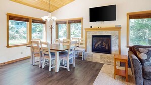 Un comedor con una mesa y sillas de madera, chimenea y televisor montado en la pared.