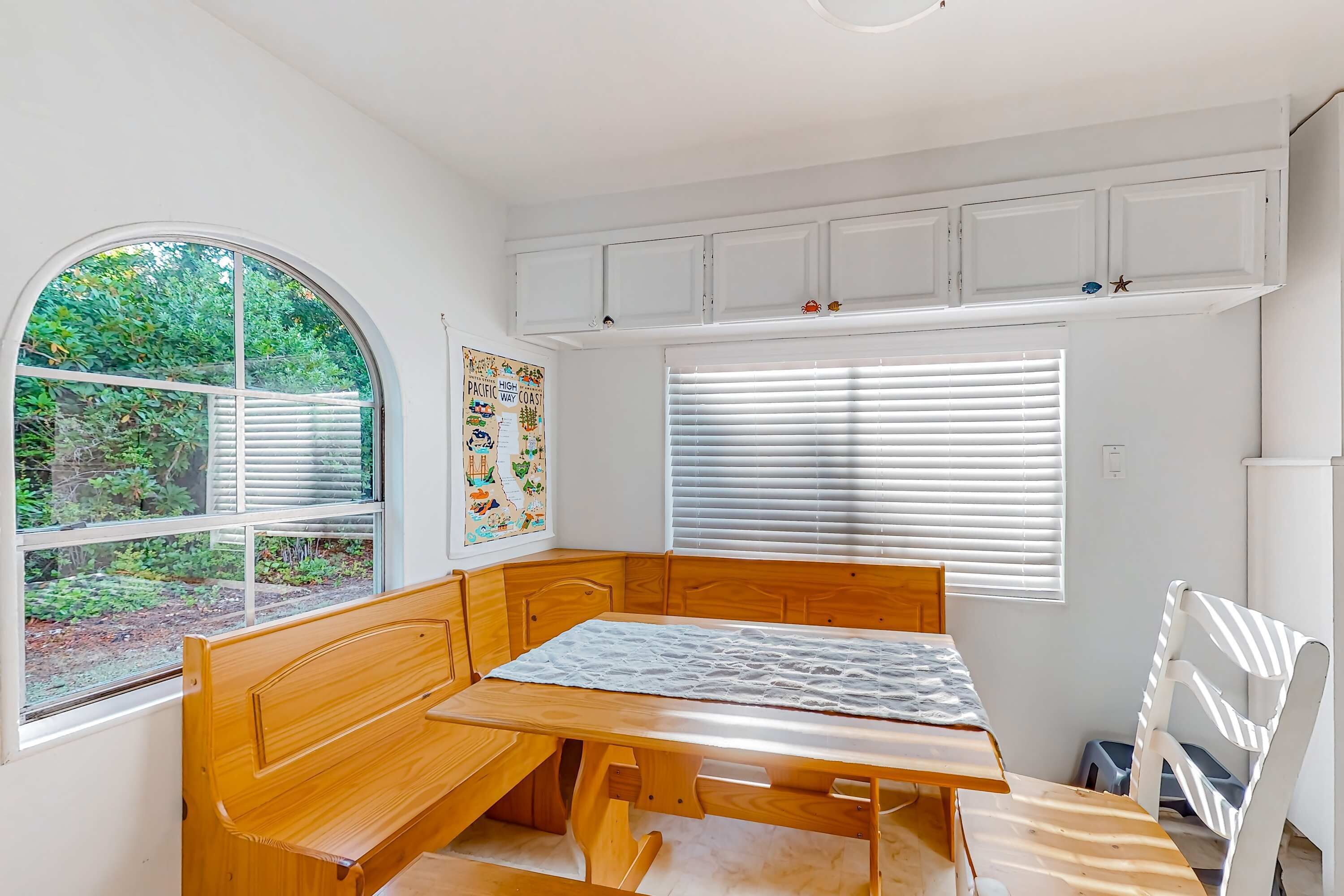 Una habitación con un banco de madera, una mesa, armarios blancos y una ventana con persianas.