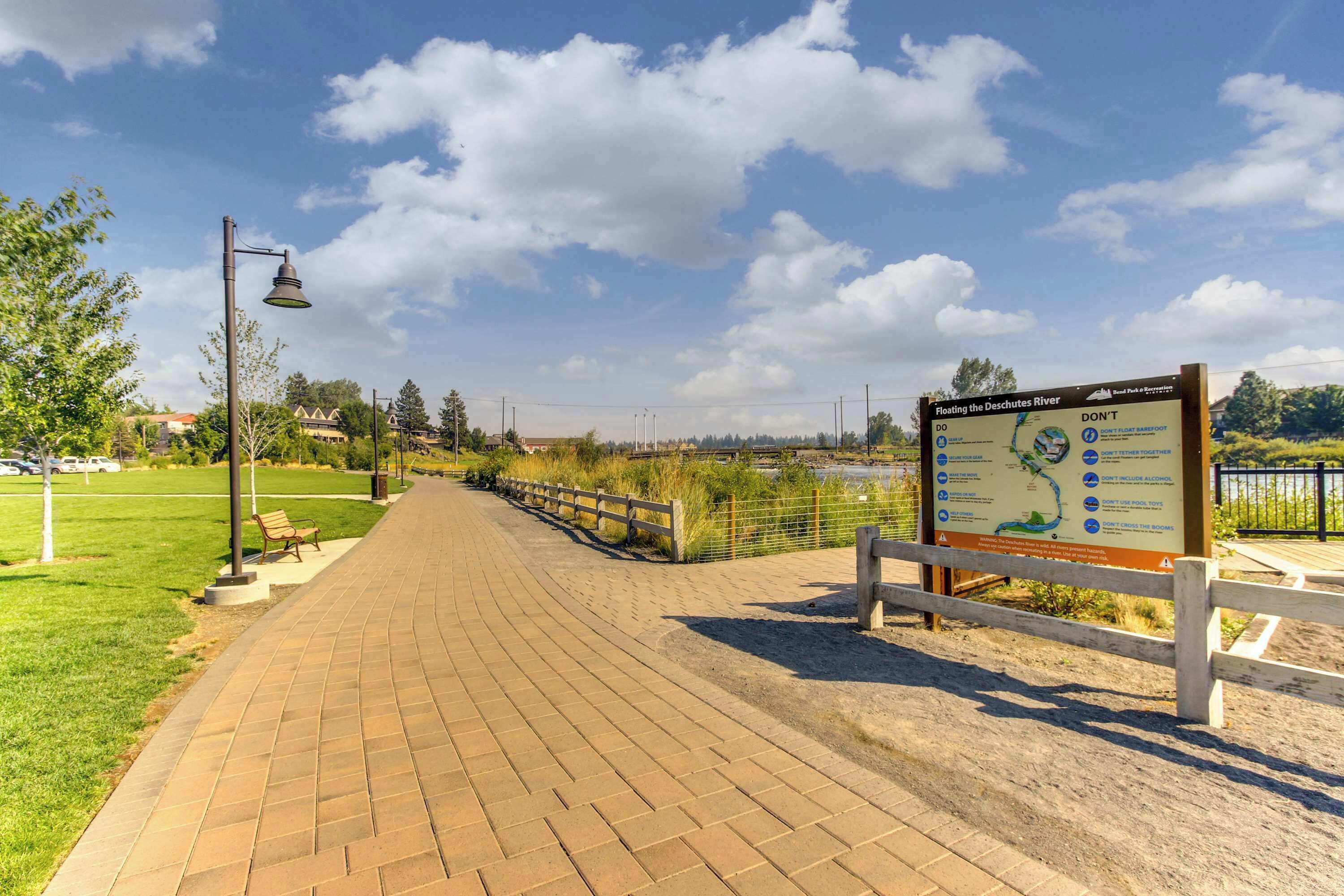 A paved walkway with a wooden fence, a bench, and a signboard.