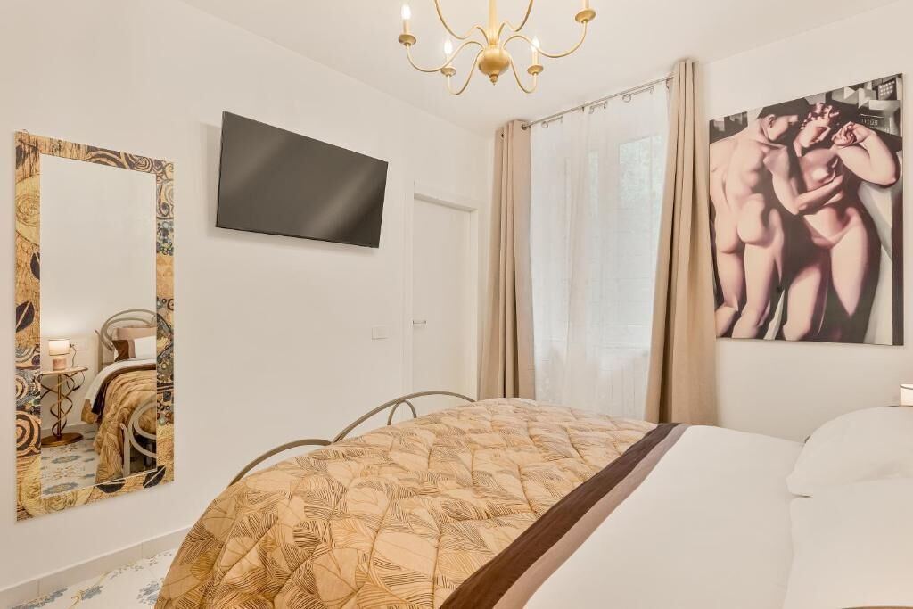 A bedroom with a bed, a TV mounted on the wall, a large mirror, and a painting.