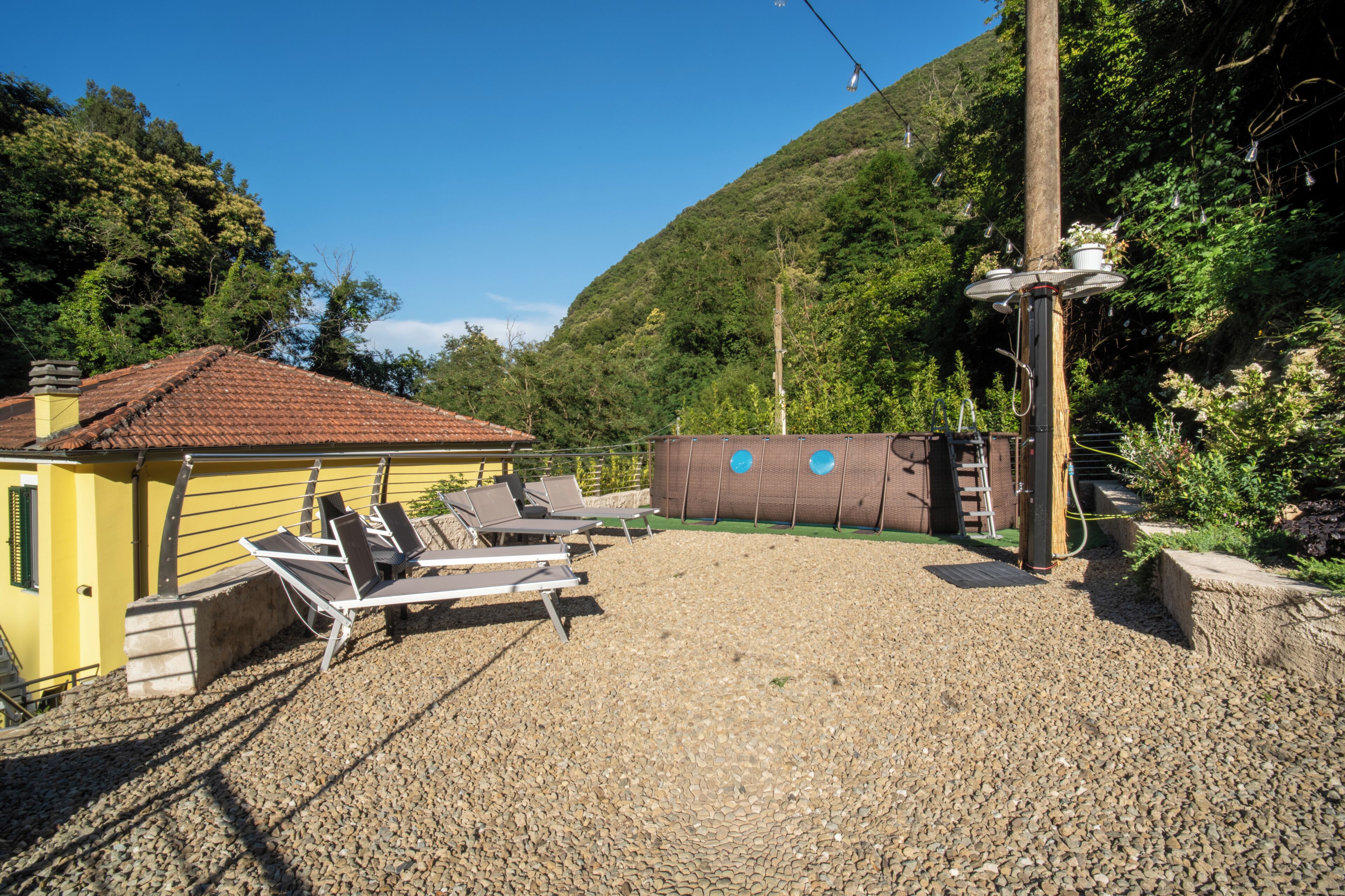 A gravel patio with lounge chairs, a yellow building, and a hill in the background.