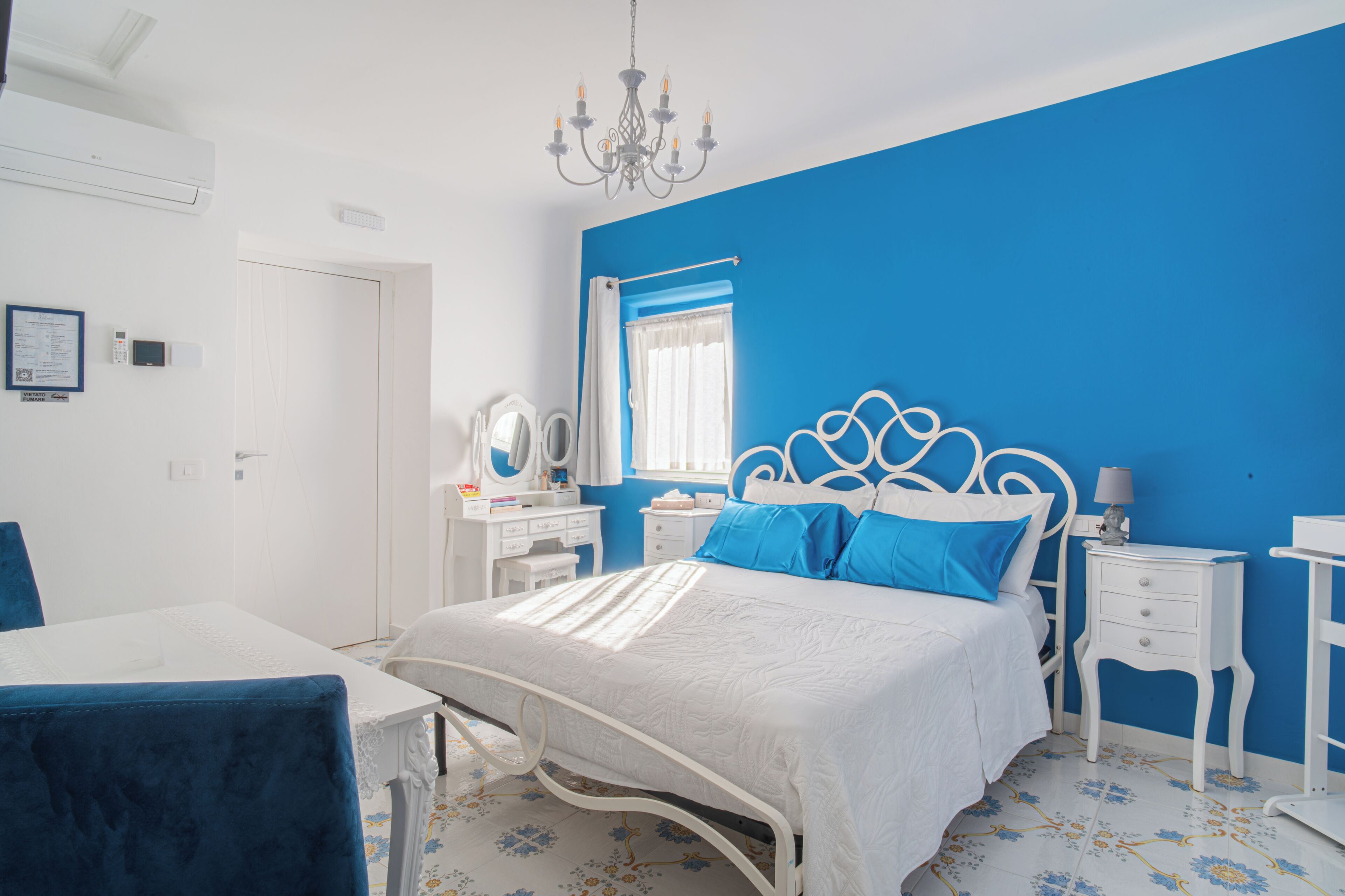 A bedroom with a bed, bedside tables, a dresser, a chair, and a chandelier.