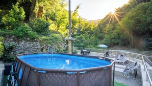 Ein rechteckiges Whirlpoolbecken, umgeben von einer Steinmauer, mit einer Rasenfläche und Liegestühlen.
