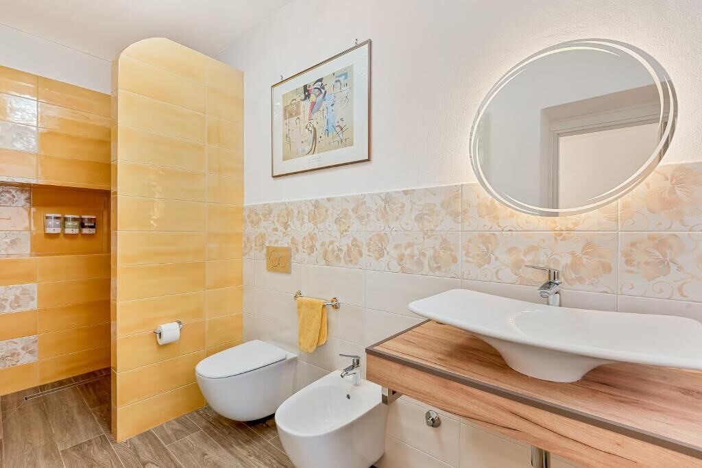 Un baño con bidé, inodoro, tocador con lavamanos y espejo con luz.