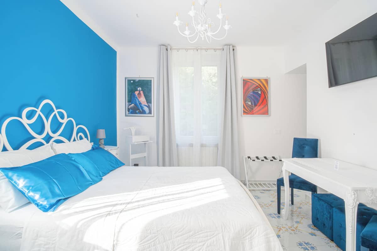Une chambre à coucher avec un lit, un bureau, une chaise, un lustre et des œuvres d’art accrochées aux murs.
