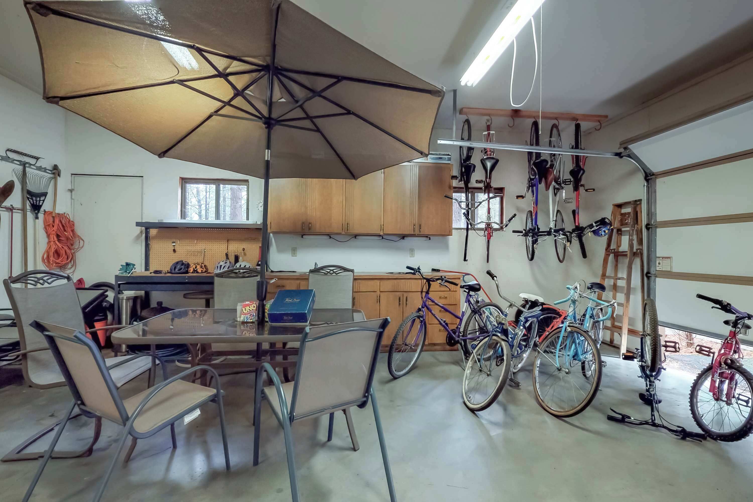 A garage with bicycles, a table with chairs, and a large umbrella providing shade.