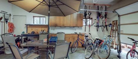 A garage with bicycles, a table with chairs, and a large umbrella providing shade.