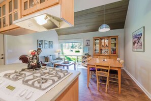 A modern kitchen with a gas stove, wooden cabinets, and a dining area with a table and chairs. - Dog-friendly condo with 6 SHARC passes & great golf course views (Sunriver)