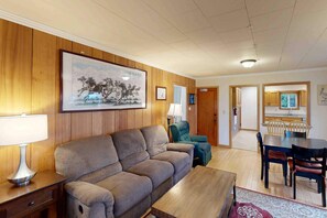 A living room with a sofa, a coffee table, a dining table with chairs, a lamp, and a framed picture on the wall. - Comfy duplex with peekaboo ocean views, private hot tub, & easy beach access (Newport)