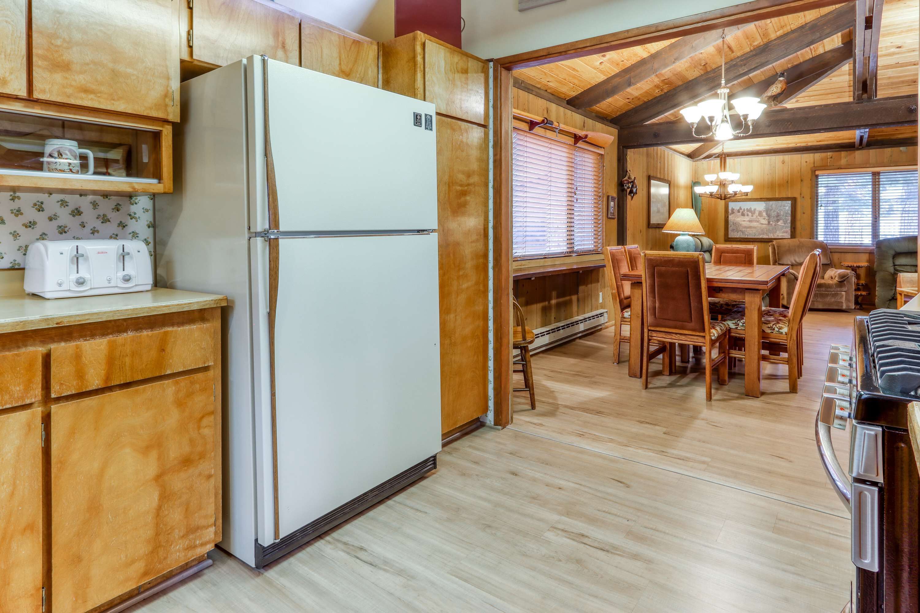 A kitchen with wooden cabinets, a refrigerator, a dining table with chairs, and a chandelier.