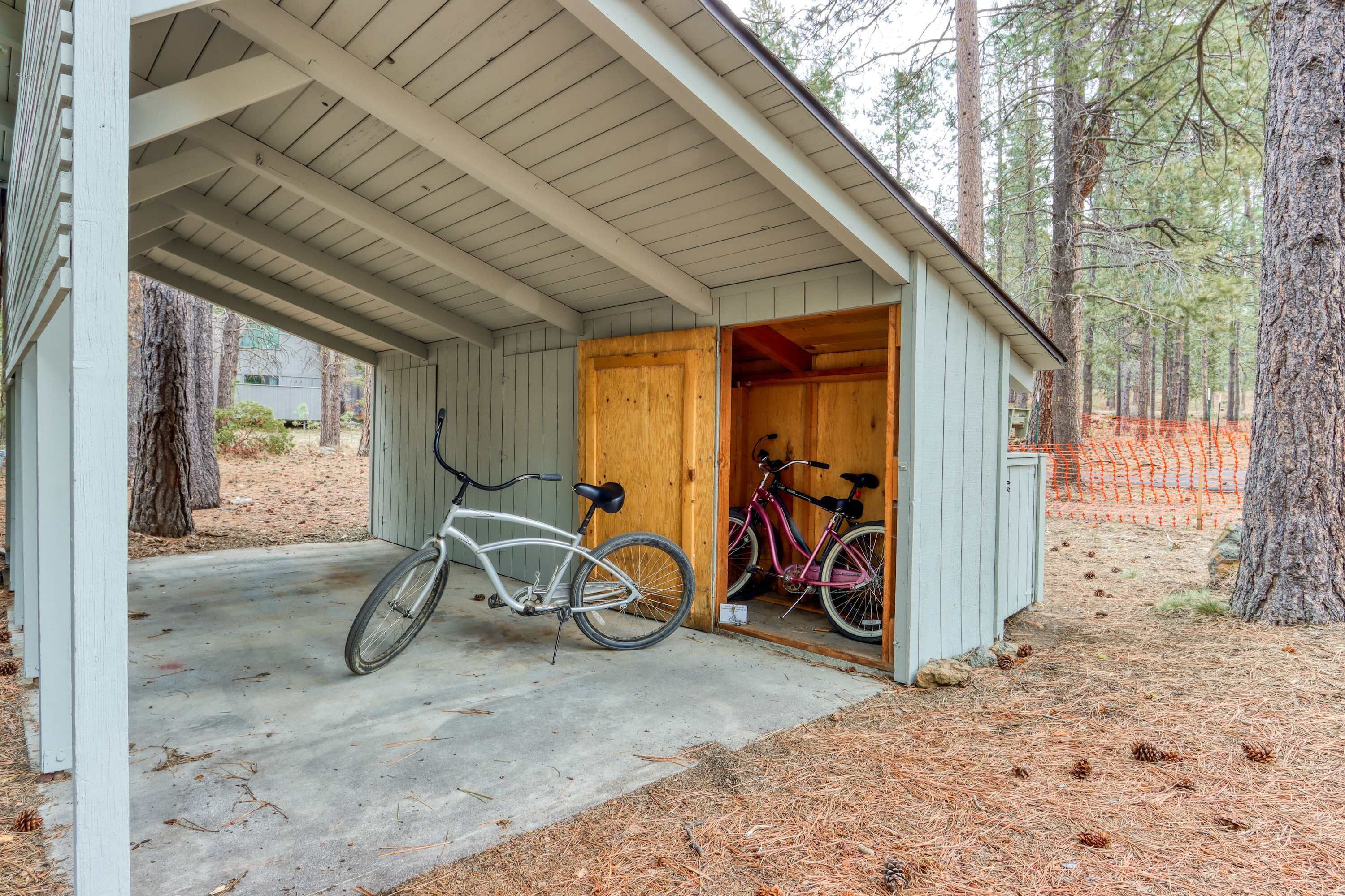 Un espace extérieur abrité avec un sol en béton, deux vélos et une structure en bois dotée d’une porte ouverte.