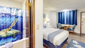 Habitación de hotel con cama, escritorio, silla, lámpara y cortina de ducha con diseño de tortuga marina.