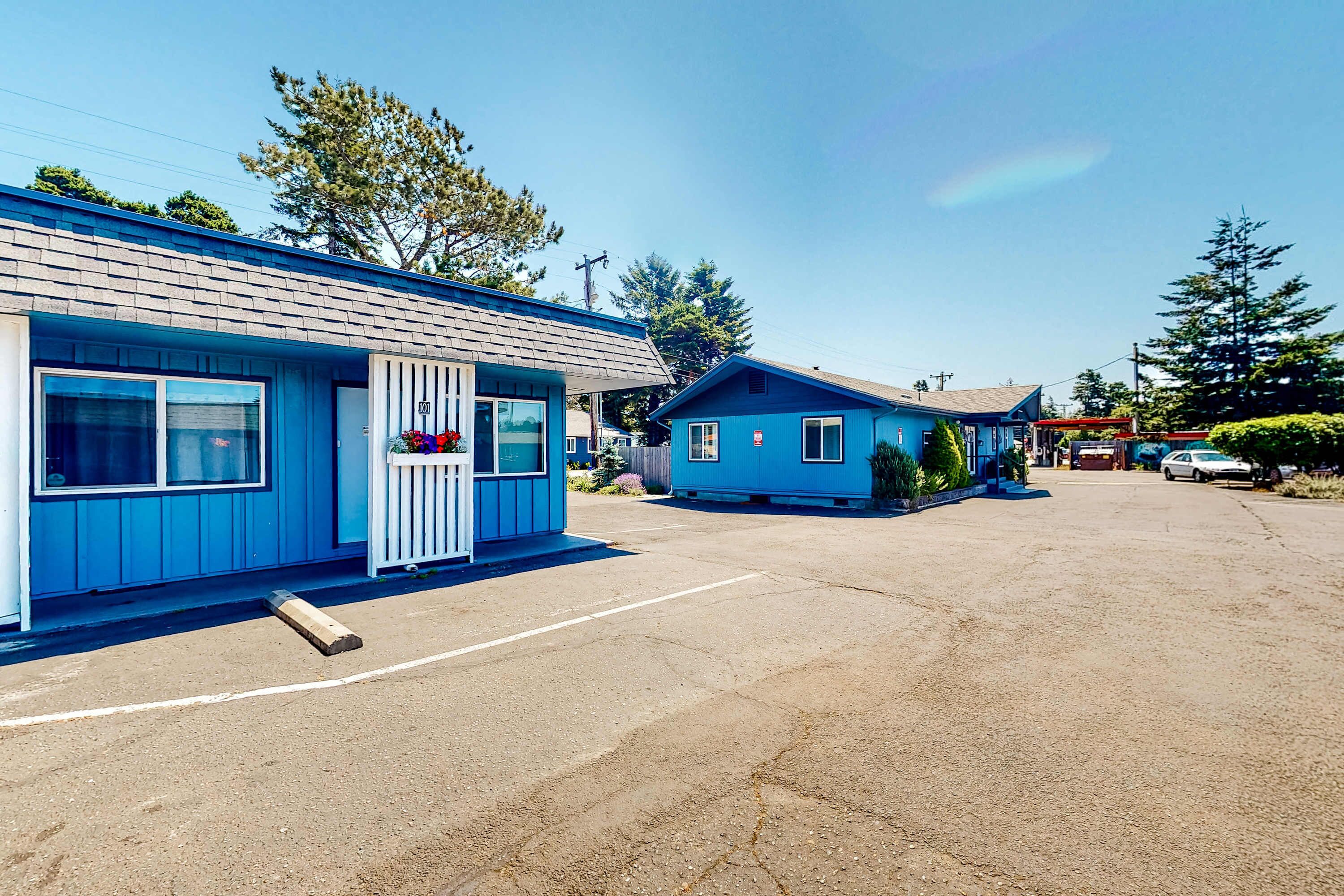 Ein Motel mit zwei blauen Gebäuden, einem Parkplatz und wolkenlosem Himmel.