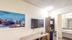 Habitación con una televisión montada en la pared, una mesita consola de madera, un refrigerador y un baño con salpicadero de azulejos.