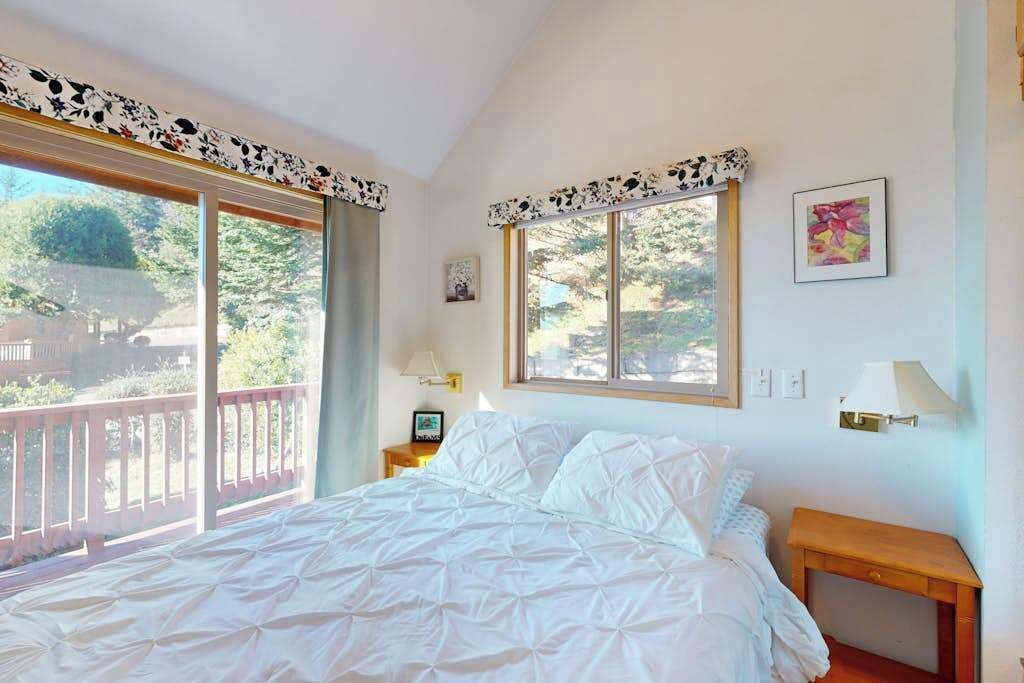 Une chambre avec un grand lit, deux tables de chevet, une fenêtre donnant sur un beau paysage et un balcon.