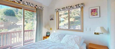 Une chambre avec un grand lit, deux tables de chevet, une fenêtre donnant sur un beau paysage et un balcon.