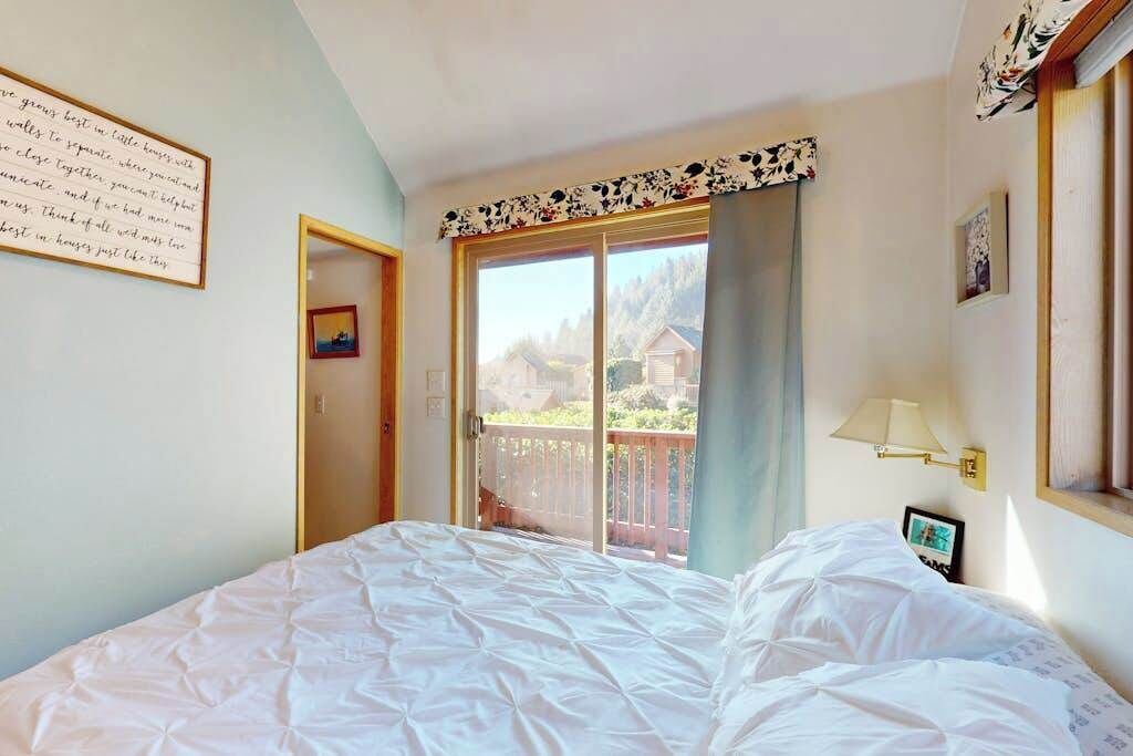 Un dormitorio con cama, ventana con vistas, puerta y lámpara de pared.