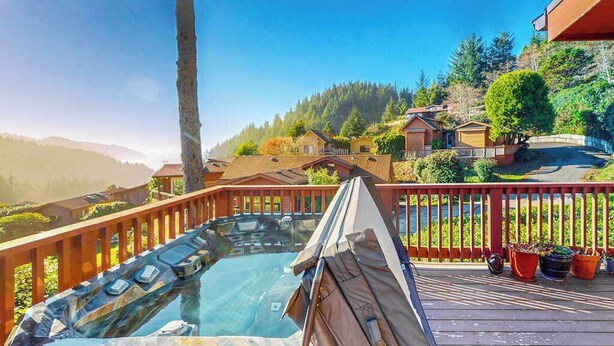 A hot tub on a wooden deck with a view of houses and trees. - Dog-friendly cabin withprivate hot tub, large deck & beautiful ocean mountain view (Brookings)
