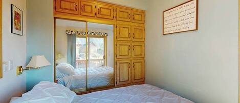 A bedroom with a bed, a wardrobe, a mirror, and a framed note on the wall.