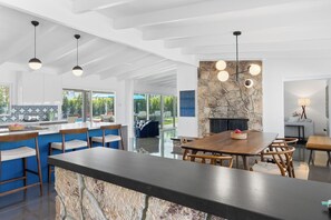 Eine moderne Küche mit einer Wand als Blickfang aus Stein, einem Essbereich mit Holztisch und -stühlen sowie Pendelleuchten.