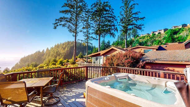 En træterrasse med jacuzzi, spisebord og stole, omgivet af et træhegn og høje træer.