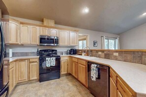 A kitchen with wooden cabinets, a black stove, a microwave, and a dishwasher. - Charming home in wooded setting with deck, BBQ grill, WiFi, and fireplace (Sunriver)